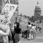 LGBTQ activists marching on the Texas State Capitol in 1978. Many people hold signs and march down the street towards the Capitol building.