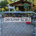 A cardboard sign on a chainlink gate that says "ABOLISH ICE!"