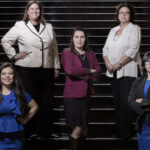 Members of the Texas House LGBTQ Caucus. Five people standing on dark and large staircase, some in blazers and slacks, others in blouses and skirts, hands on hips or arms crossed.