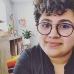 Stefanía García smiling at camera with short curly hair and glasses.