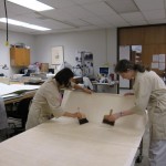 Lew and Watkins place a large sheet of Japanese paper on the table before it is applied to the poster.