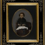 Boy in a Dress. Unidentified photographer. Oil on tintype. Ca. 1875. Greek Revival style frame.