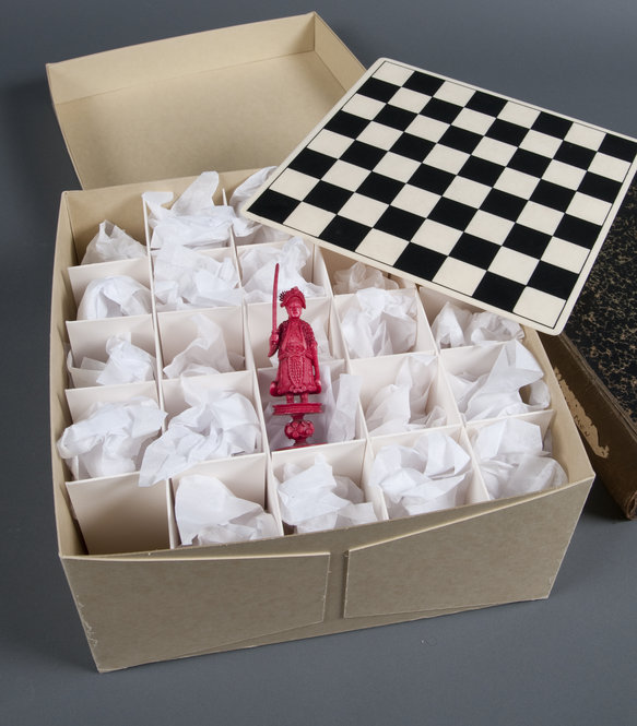 This chess set was owned by Ezra Pound and was acquired as part of the Marcella Spann Booth collection. The individual chess pieces are wrapped in tissue paper, and the board sits on top of an acid-free mat board grid. The original box for the set is pictured under the board. Photo by Pete Smith.