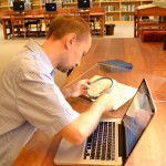 Dariusz Pachocki uses a magnifying glass to read a manuscript in the Lesiman papers in the Ransom Center's reading room. Photo by Alicia Dietrich.