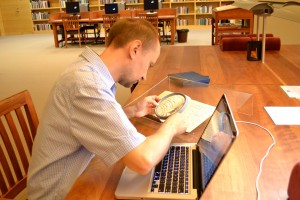 Dariusz Pachocki uses a magnifying glass to read a manuscript in the Lesiman papers in the Ransom Center's reading room. Photo by Alicia Dietrich.