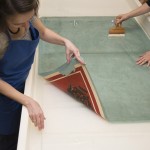 Conservators placing the lined poster into a large bath of deionized water. Here we see the back of the lining and one corner of the front of the poster. Photo by Pete Smith.