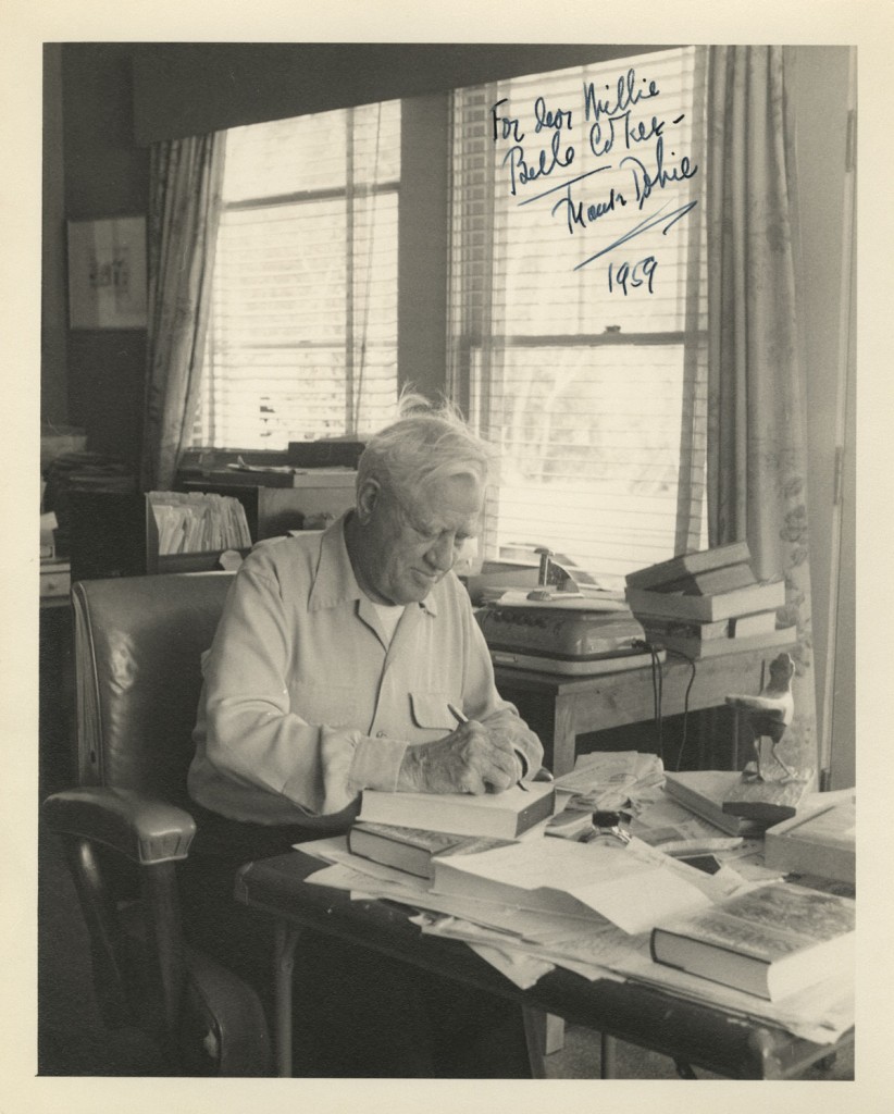 C. H. Dykeman,  Photograph of J. Frank Dobie at his desk, 1959. Note the wooden roadrunner on his desk and the open file cabinet drawer showing folders of papers.