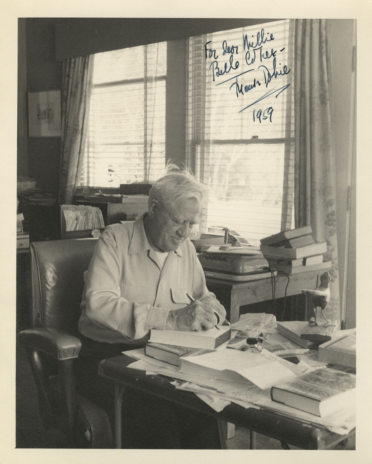 C. H. Dykeman, Photograph of J. Frank Dobie at his desk, 1959. Note the wooden roadrunner on his desk and the open file cabinet drawer showing folders of papers.