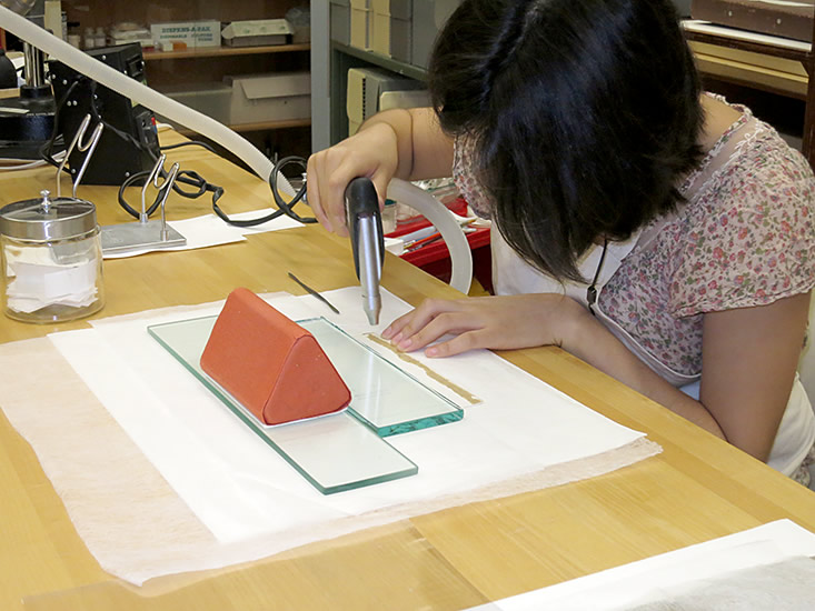 Diana Diaz using the "preservation pencil" to detach the kraft-paper tape.