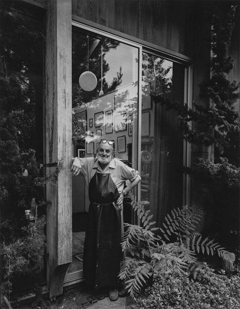 Black and white photographic portrait of a man standing in front of a large sliding glass door