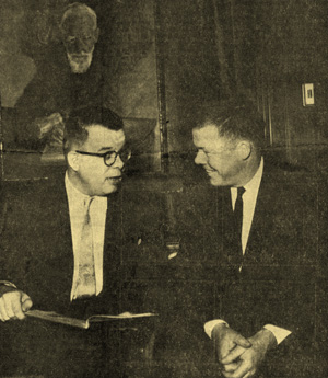 William Todd and F. Warren Roberts discuss a rare book beneath a portrait of George Bernard Shaw, ca. 1961. Unidentified photographer.