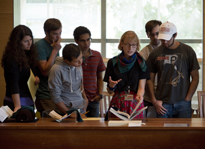 Graduate intern Jenn Shapland, center, shares annotated books from Wallace’s library and research materials he used while writing “Infinite Jest.” Photo by Pete Smith.