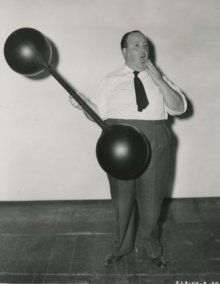 "Heavyweight in Light Mood" publicity still of Hitchcock toying with a prop on the set of “Rebecca.”