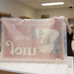 Conservators remove the poster from the bath. They are able to handle the wet paper because it is layered between strong sheets of spun polyester, called Reemay. The poster clings to the Reemay as it is pulled from the water. Photo by Pete Smith.
