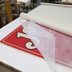 After bathing, the poster is placed between layers of spun polyester and wool felts to allow it to dry flat. A rigid board is laid over the felts and weights are added. It will stay this way for about a week. Photo by Heather Hamilton.