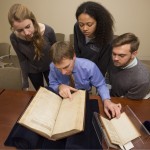 Elon Lang, seated in the center, and undergraduates from "Drama in the Archives" view collection materials. Students, clockwise from upper left, are Lily Pipkin, Haley Williams, and Kenneth Williams. Photo by Pete Smith.