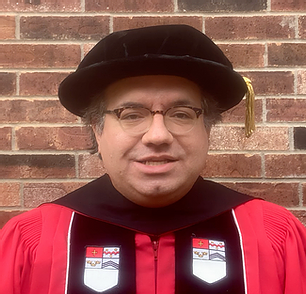 Image of Kenneth Fleischmann, wearing a doctoral regalia, standing in front of a brick wall