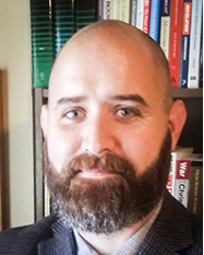 Portrait of Nathan Leach, a white man with dark hair and a beard, dressed in a dark suit.