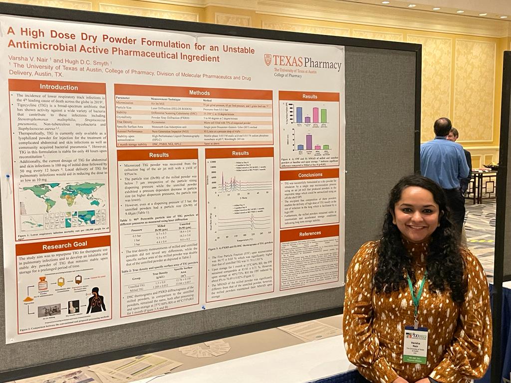 Varsha Nair standing in front of her research poster after presenting her work on high dose dry powder formulations for unstable antibiotics.