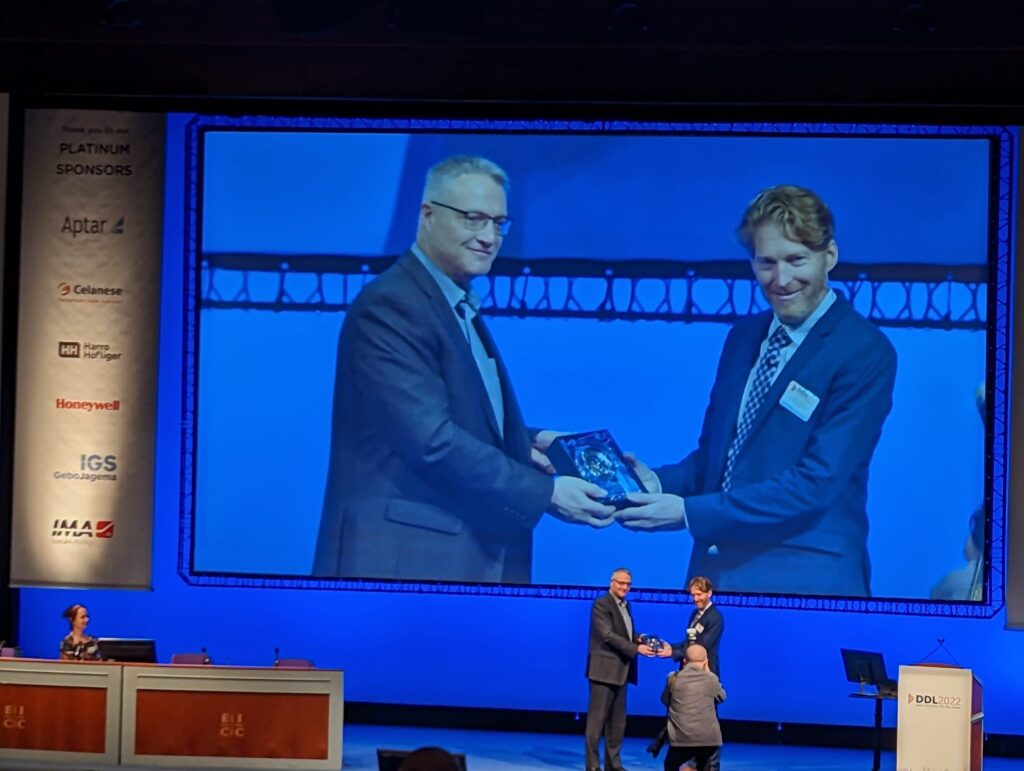 Dr. Smyth standing on a stage and receiving an award (Smyth Lab at DDL 2022 received the lecture award).