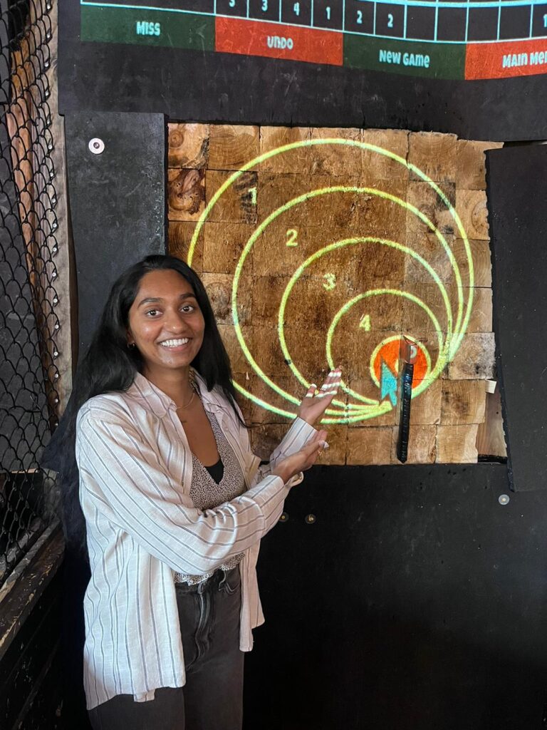 Nila points to axe she threw that is embedded in target.