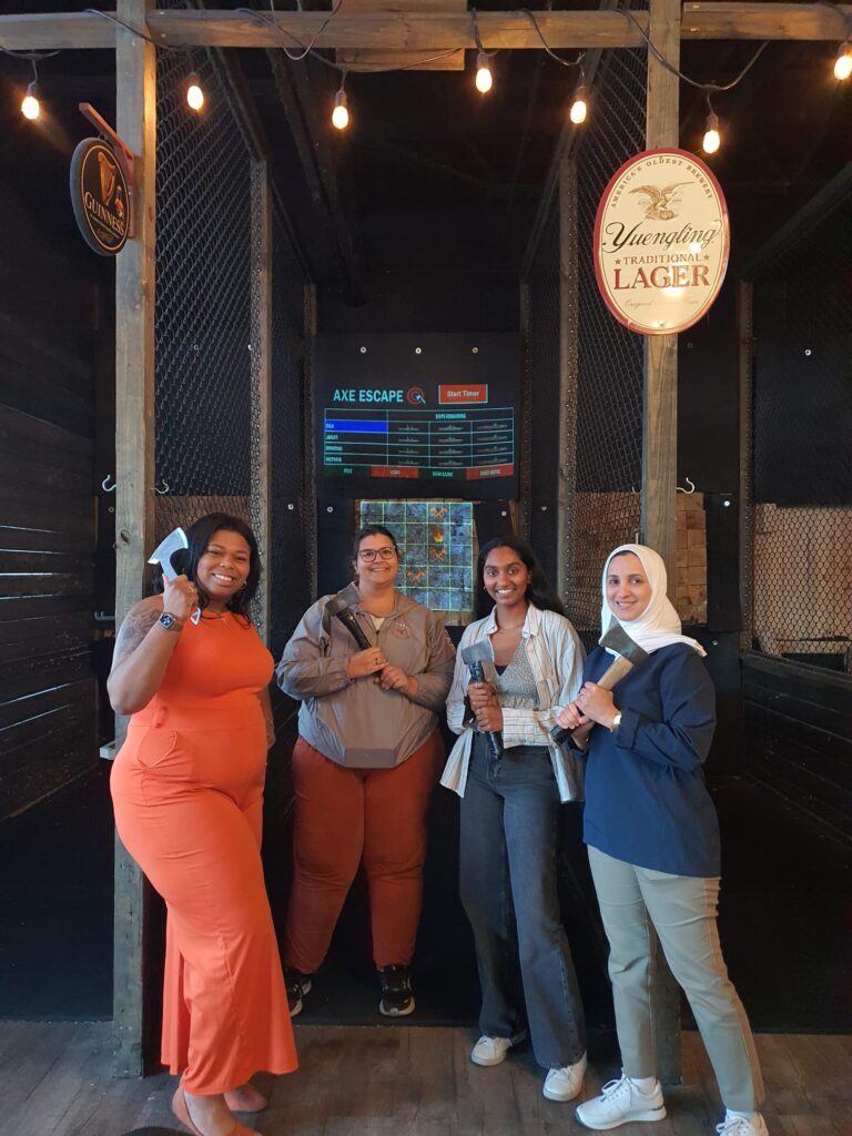 Axe throwing competition between lab members Jailen, Nila, and Rowidah. Visiting Ph.D. student from Brasil, Victoria, is also in photo.