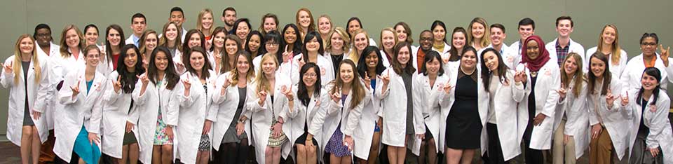 a group of students in white lab coats doing the Hook Em sign