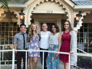 Five students wearing dressy clothes and standing in front of a house or restaurant