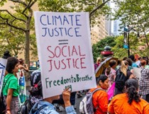 A group of peaceful demonstrators in an outdoor setting. Sign reads, "Climate Justice = Social Justice. Freedom to Breathe."