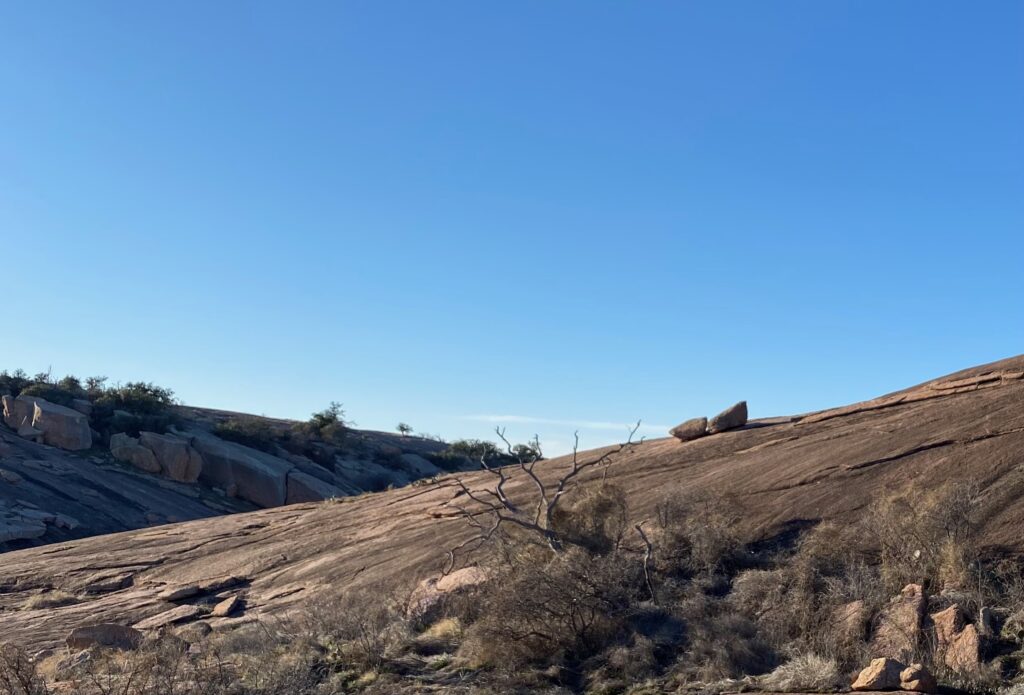 Top of Enchanted Rock and hills beyond, with clear, blue sky.