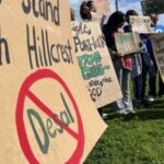 Group of protestors standing on the grass holding hand-lettered signs.