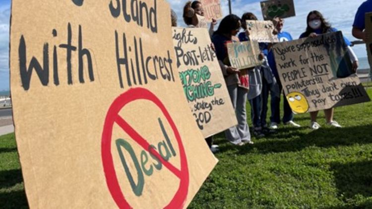 Group of protestors standing on the grass holding hand-lettered signs.