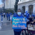 Protesters rally for clean drinking water in front of a government building in Sacramento, wearing blue t-shirts and carrying signs.