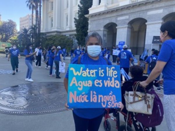 Protesters rally for clean drinking water in front of a government building in Sacramento, wearing blue t-shirts and carrying signs.