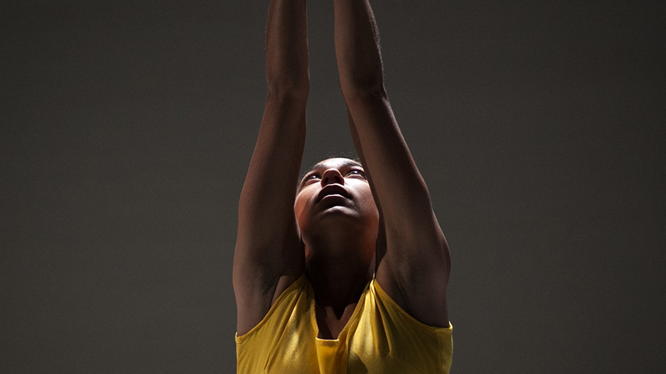 a performer looks up at their arms, stretched over their head