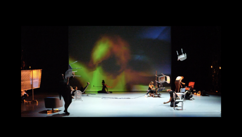 dancers are spread out on a stage, interacting with chairs that are floating and recording each other with camera phones