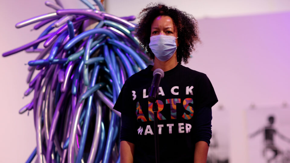 Woman with curly brown hair wearing a mask and a shirt that says "Black Arts Matter"