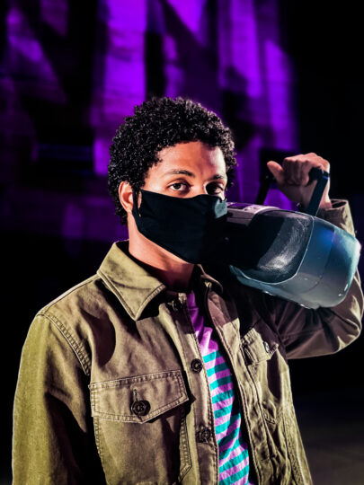 man with dark, curly hair wearing a black mask and holding a boombox