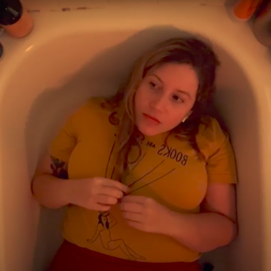 woman with blonde hair and a yellow shirt lies down in her bathtub
