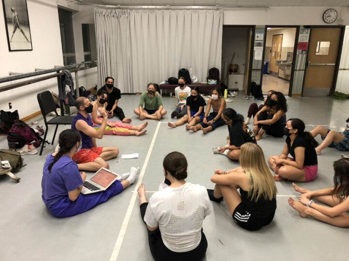 group of dancers sit around a choreographer