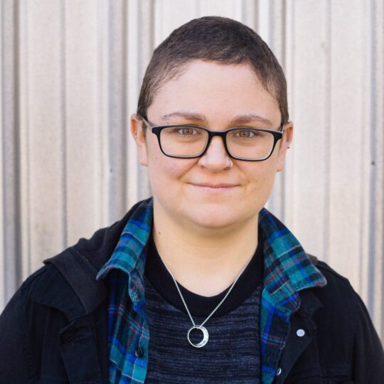 artist with rectangular glasses frames and short brown hair wearing a blue flannel