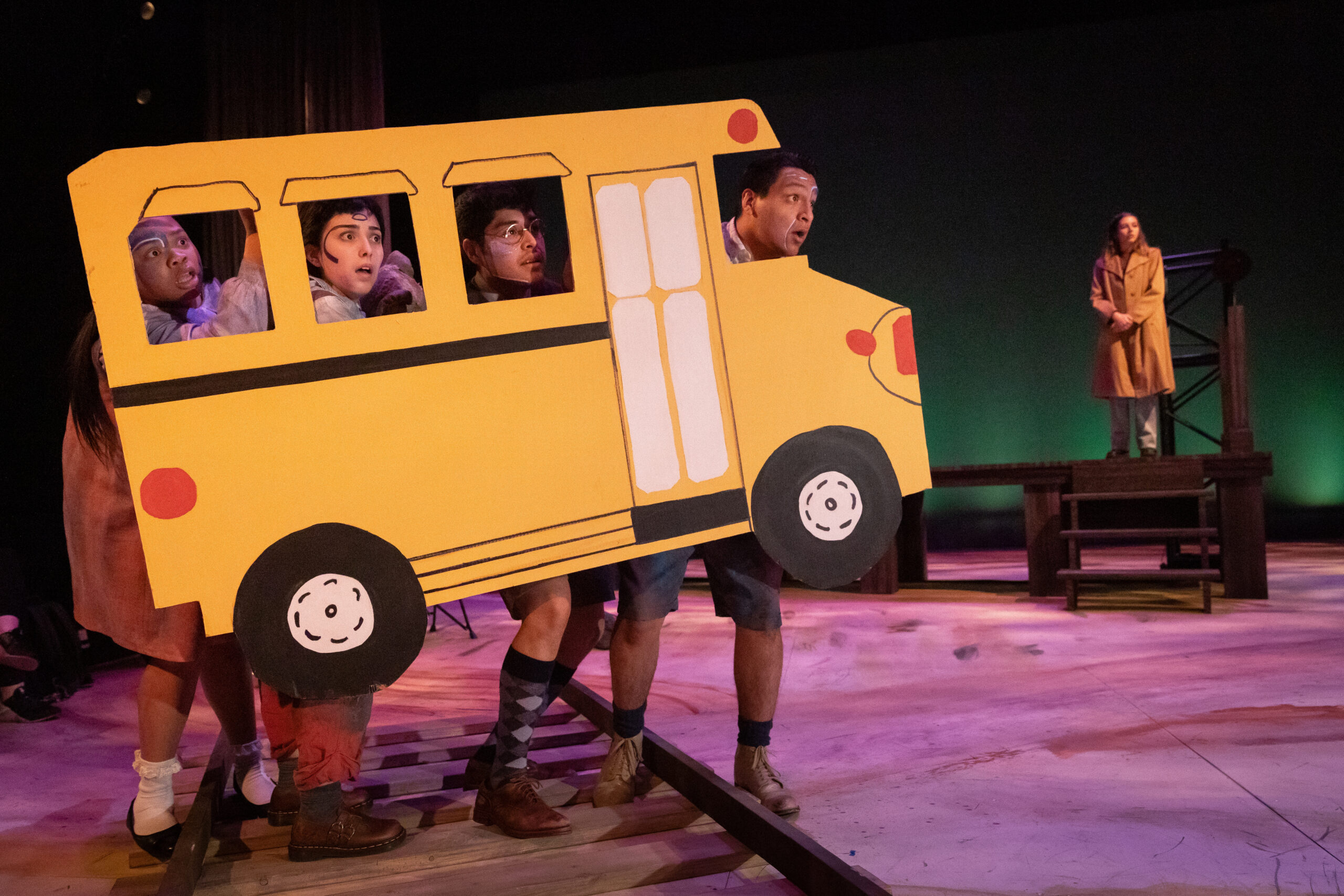 four actors portraying "ghost children" peer out of the windows of a paper school bus
