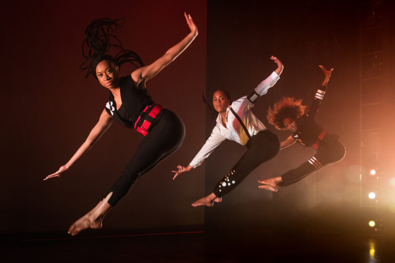 three dancers captured mid-jump with their feet pointed and their arms outstretched