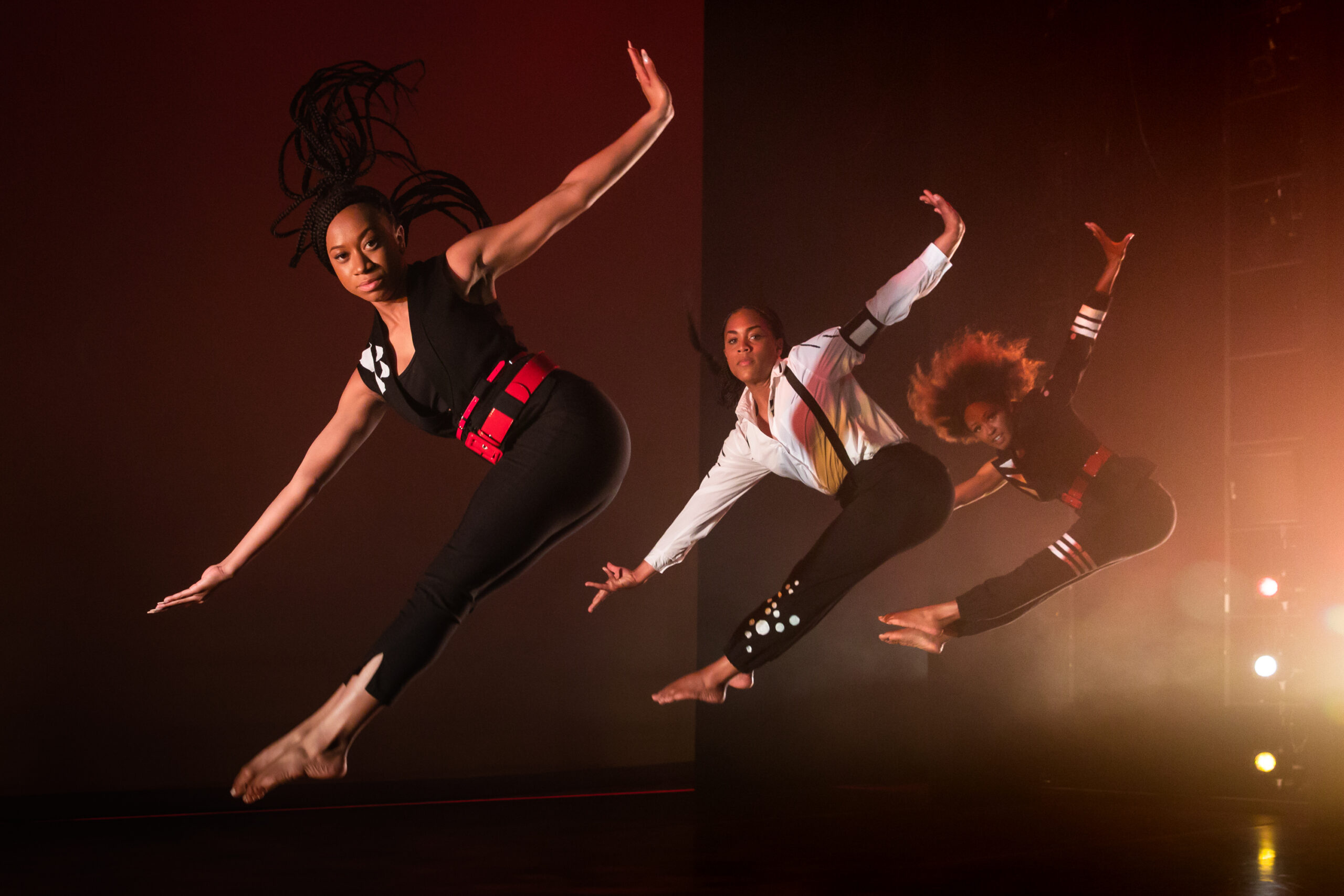 three dancers captured mid-jump with their feet pointed and their arms outstretched