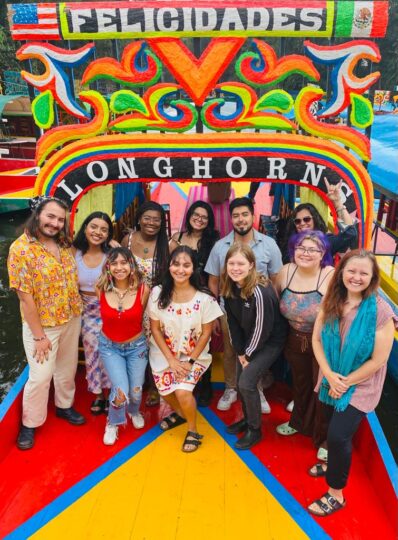 a group of eleven students and faculty pose in front of a colorful archway featuring the words "Felicidades Longhorns"