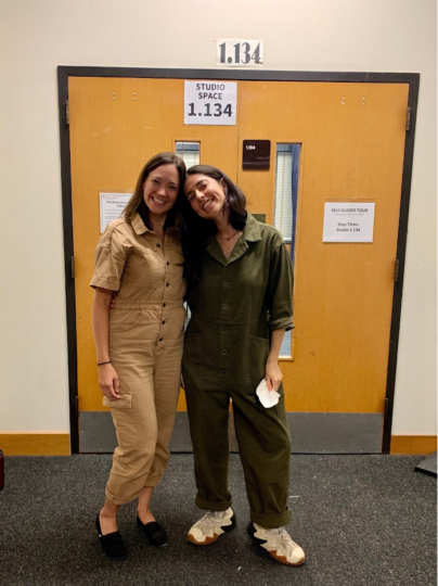 Jenny Lavery and Justine Gelfman, in coordinating jumpsuits, grin and embrace outside a rehearsal room. 