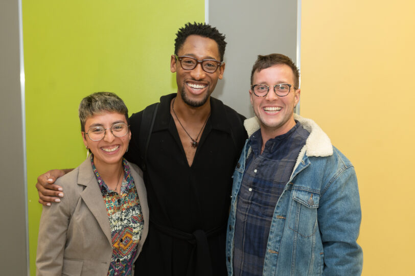 three people stand posing for the camera, smiling with their arms around each-other