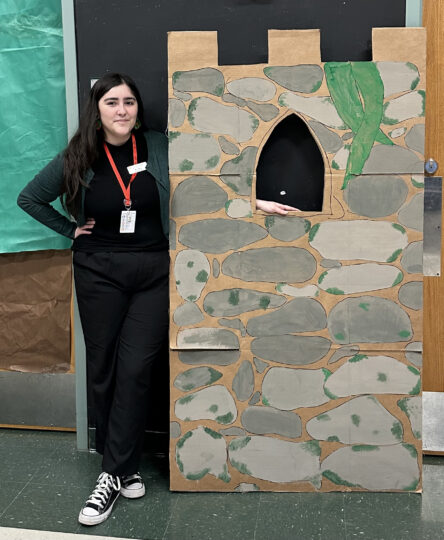 UTeach Theatre student teacher Davina Silva poses next to a cardboard set piece that's made to look like a castle tower