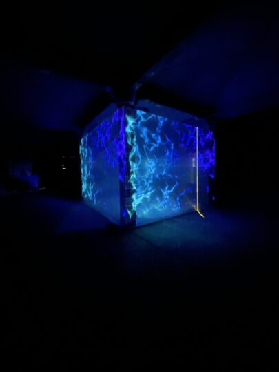 Four columns wrapped in material forming a large cube with vibrant blue projections on it