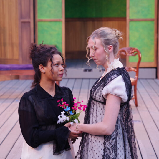 Nya Garner and Sophie Anne Miller perform a scene from SENSE AND SENSIBILITY, facing each other and holding hands with a flower bouquet between them